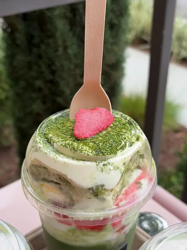 Strawberry tiramisu matcha in a clear cup, dusted with matcha and topped with a freeze-dried strawberry