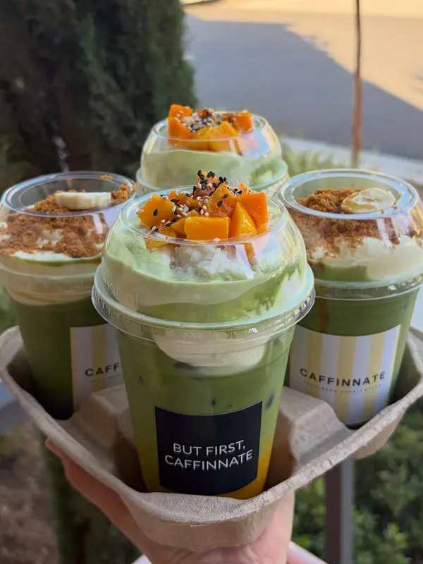 Three iced mango matcha drinks in Caffinnate cups with mango on top