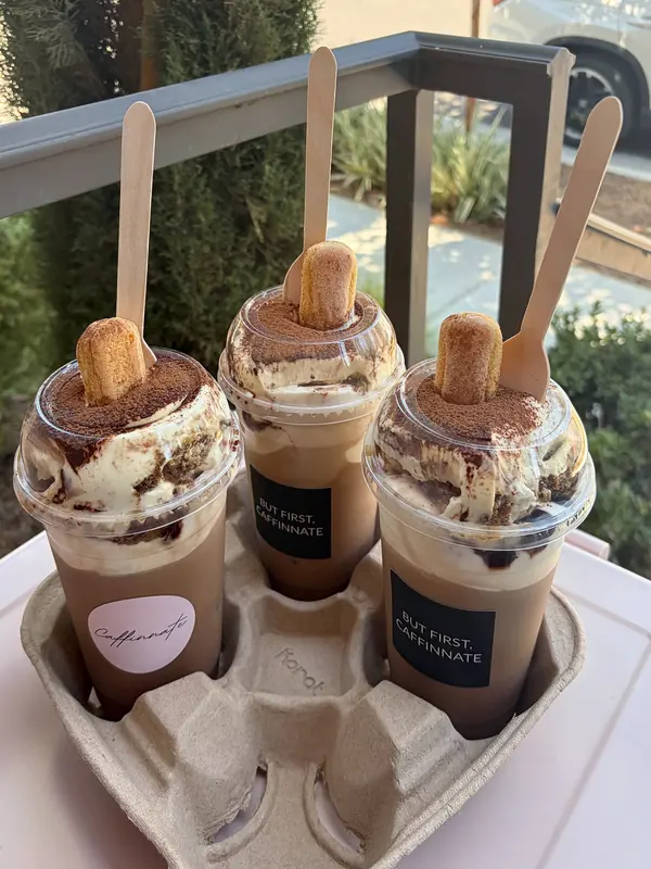 Three tiramisu lattes topped with cream, cocoa dust and a ladyfinger cookie